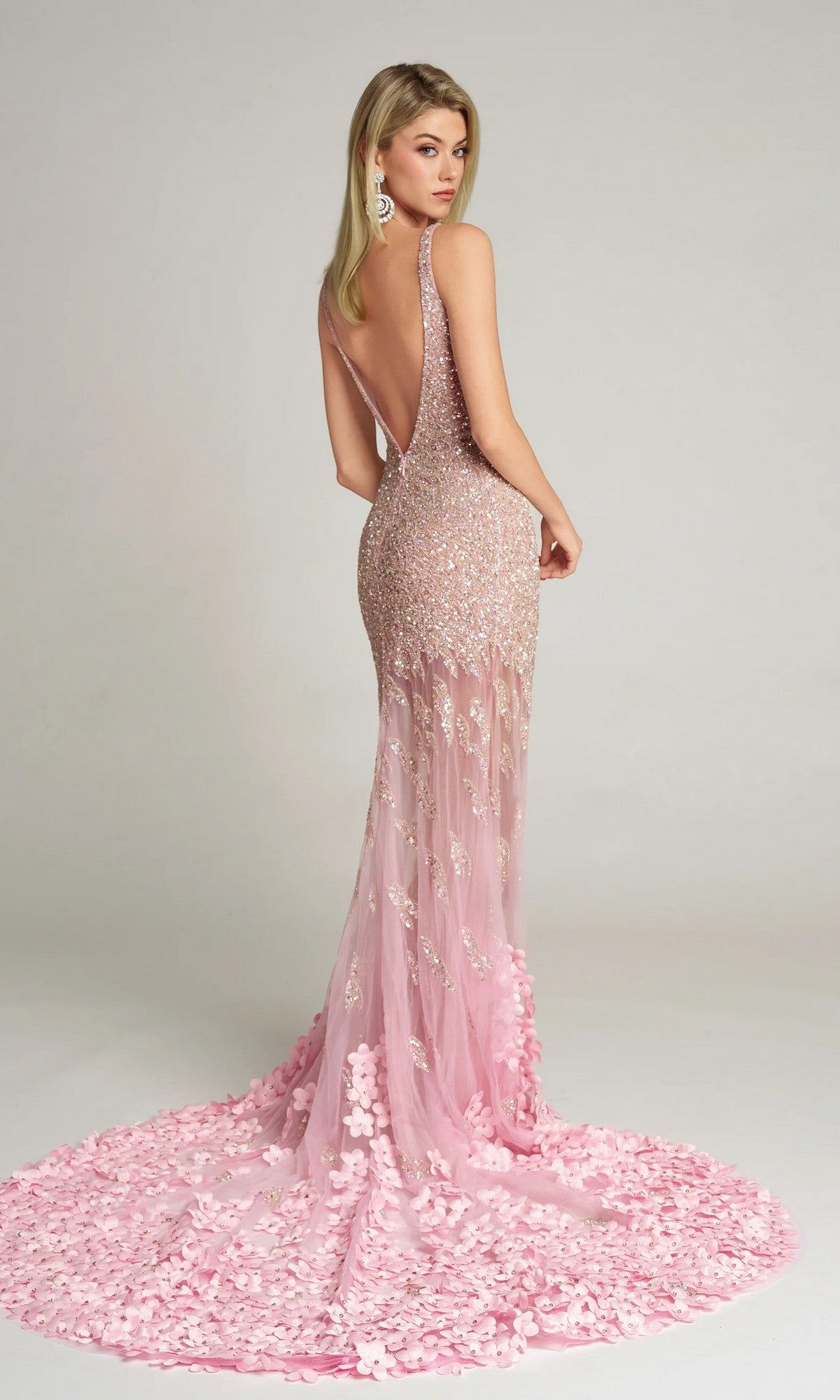 A woman poses with her back to the camera in the Portia and Scarlett PS25987C, a sleeveless, backless, floor-length pink formal dress adorned with floral embellishments.